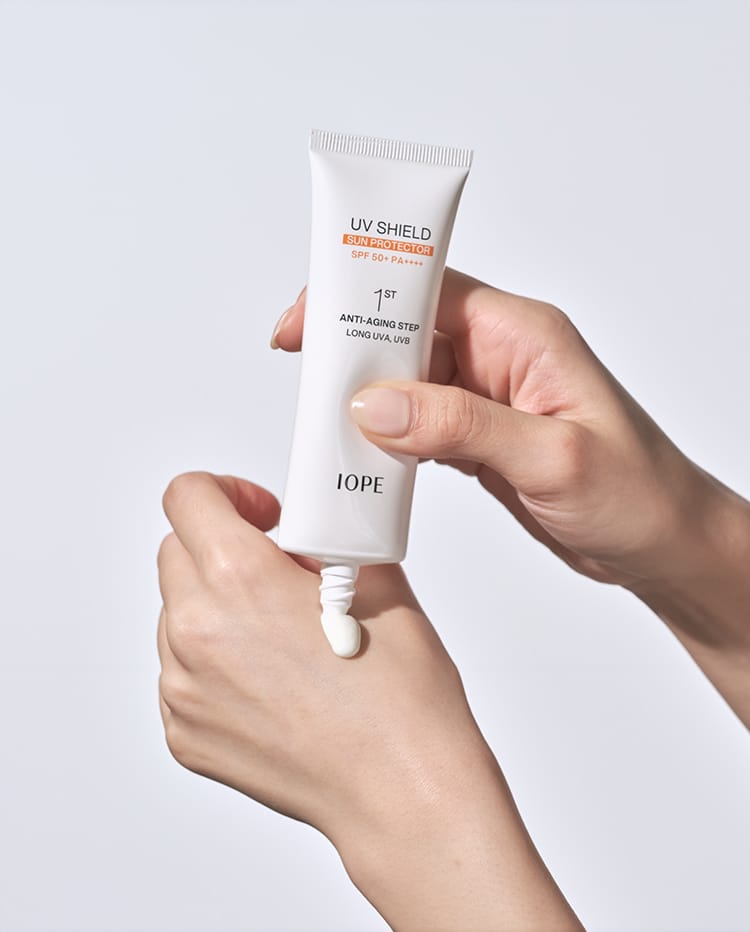 아이오페 UV 쉴드 선 프로텍터 SPF 50+ PA++++ 퍼스트 안티 에이징 스텝 롱 UVA, UVB를 손에 덜어내고 있다.
